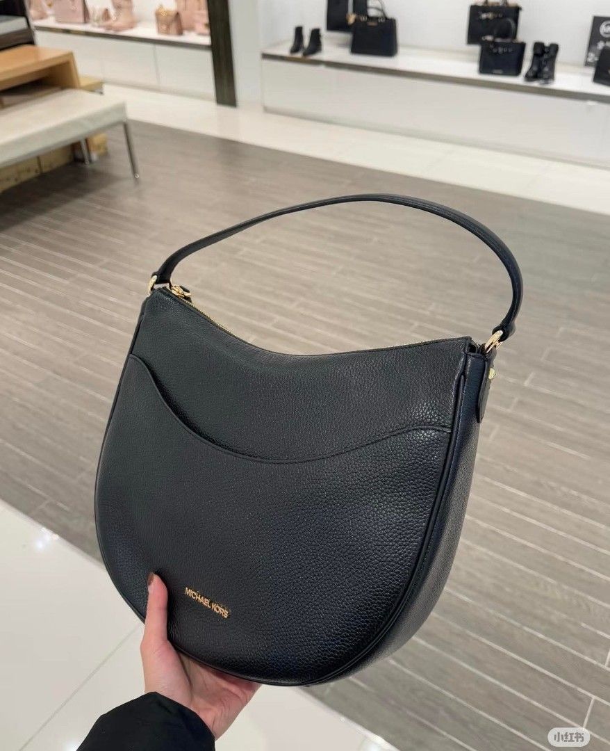 Michael Kors Dover Large bag (Category: Other Accessories) located in Rizal. Submitted by vanbdc24 (Listing ID 1432716525, Image 2). Description: Stylish Michael Kors crescent shoulder bag. Features a curved design with a single shoulder strap. Available in black, brown, and a light pink/cream MK pattern. The bag has a zip closure and a small pocket on the front. The Michael Kors logo is visible on the front of the bag..