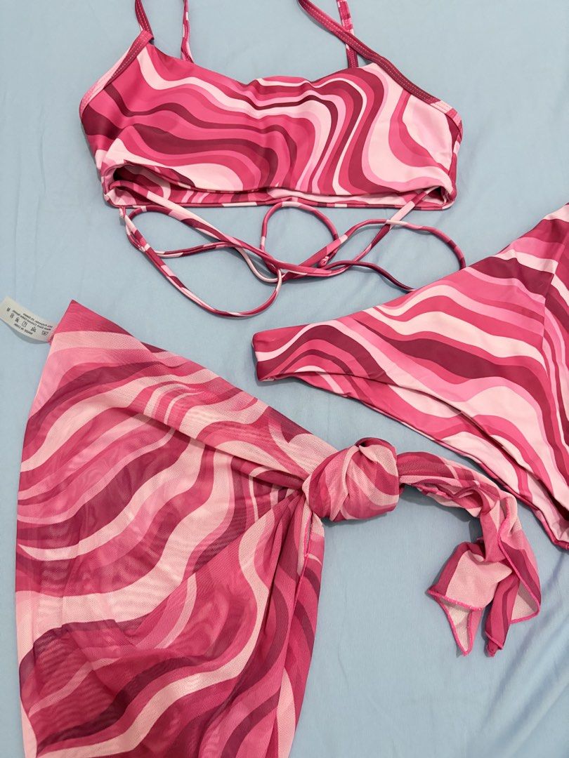 SHEIN Swim Bikini Set with Sarong (Category: Bikinis & Swimsuits) located in Muntinlupa City. Submitted by closetfinds_ph_952 (Listing ID 1432737158, Image 3). Description: - SHEIN Bikini Set - Size: Medium - Includes: Top, Bottom, and Sarong - Design: Pink wave pattern - Top: Adjustable straps, wrap-around tie - Bottom: High-cut style - Sarong: Can be tied around the waist.