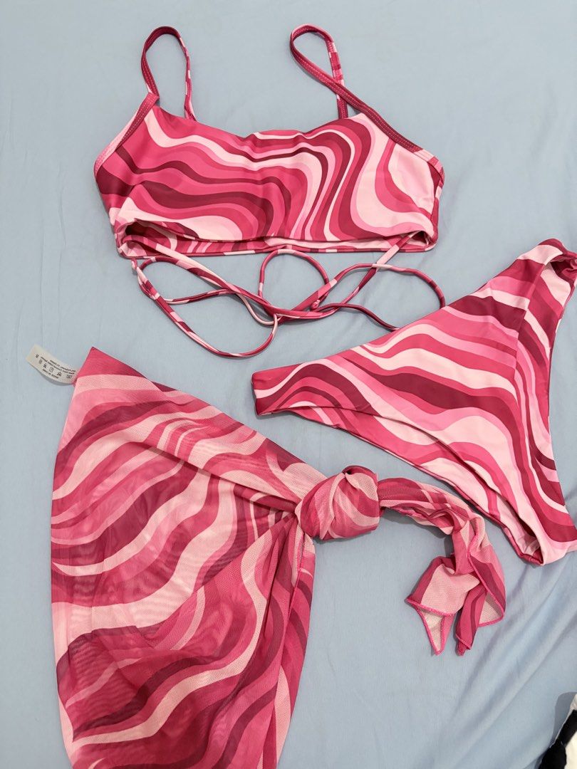 SHEIN Swim Bikini Set with Sarong (Category: Bikinis & Swimsuits) located in Muntinlupa City. Submitted by closetfinds_ph_952 (Listing ID 1432737158, Image 1). Description: - SHEIN Bikini Set - Size: Medium - Includes: Top, Bottom, and Sarong - Design: Pink wave pattern - Top: Adjustable straps, wrap-around tie - Bottom: High-cut style - Sarong: Can be tied around the waist.