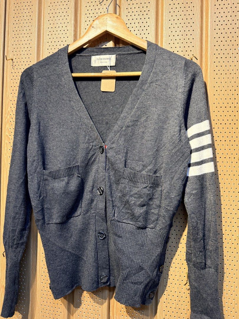 Thom Browne Grey Cardigan (Category: Luxury Apparel) located in Santiago. Submitted by twicebutnice03 (Listing ID 1432611993, Image 2). Description: - Thom Browne grey cardigan - V-neck design - Button-down closure - Two front pockets - Signature white stripes on left sleeve - Cuffs with red, white, and blue accents - Brand label visible Size & Dimes:MEDIUM-LARGE 18”23.