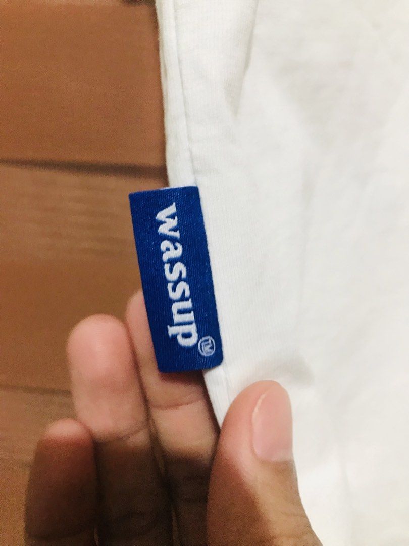 Wassup White T-shirt (Category: Tshirts & Polo Shirts ) located in Rizal. Submitted by drthriftfour (Listing ID 1432616357, Image 2). Description: - White Wassup T-shirt - Made of 100% cotton - Features a small blue Wassup logo on the front - Made in China - Approximately 24 inches in length - Crew neck and short sleeves.
