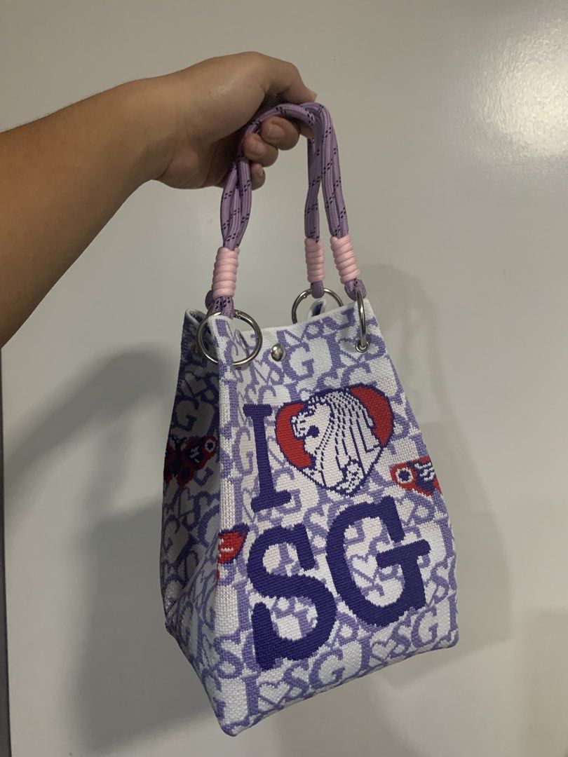 Explore I SG Handbag (Category: Tote Bags) located in Quezon City. Submitted by 47thclothing (Listing ID 1432914680, Image 2). Description: - Unique bucket bag design - Features "I SG" letters and heart patterns - Color scheme: White and purple - Handle accents: Pink and purple - Includes "Explore" tag.