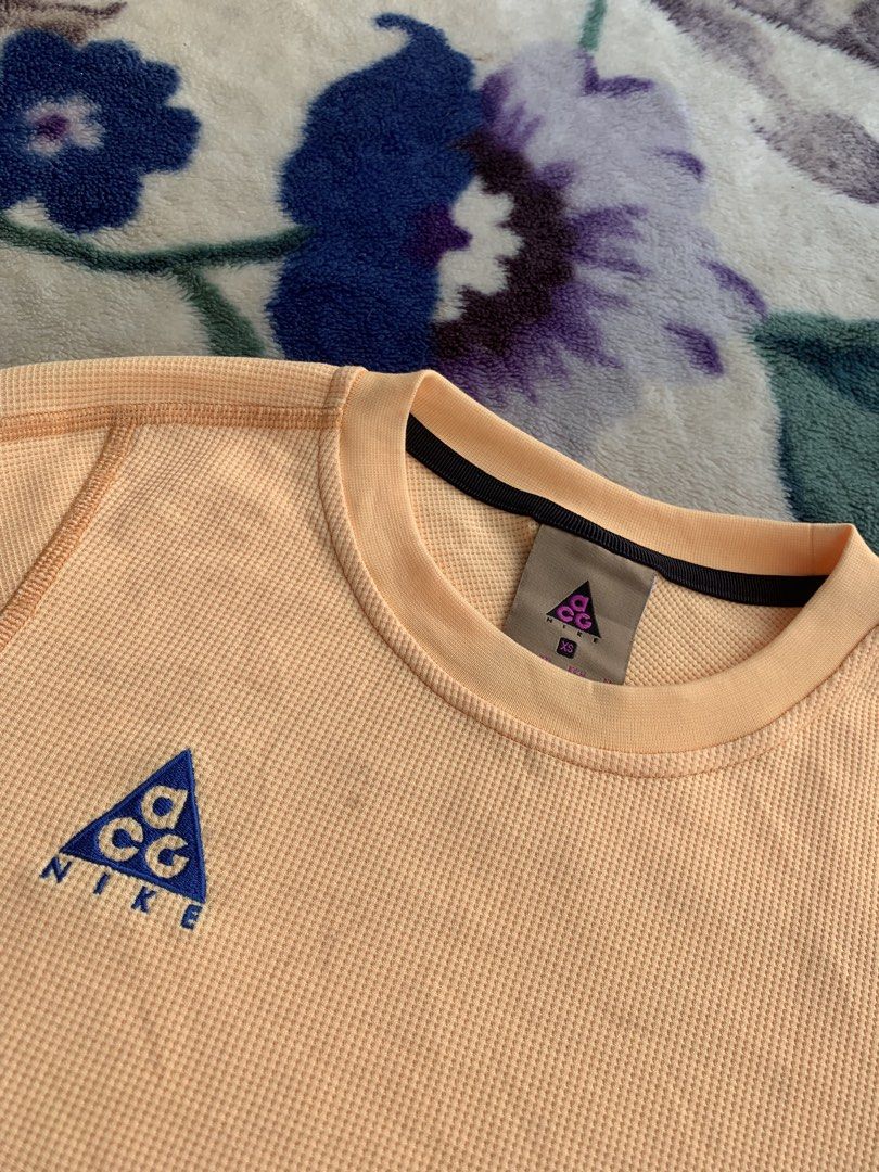 Nike ACG Long Sleeve Shirt (Category: Longsleeves) located in Cantilan. Submitted by randomthrift009 (Listing ID 1432904059, Image 2). Description: - Nike ACG long sleeve shirt - Vibrant orange color - Waffle knit texture - Crew neck design - Thumb holes on cuffs - Small Nike ACG logo on chest - Contrasting stitching detail - Minor stains present Washable .