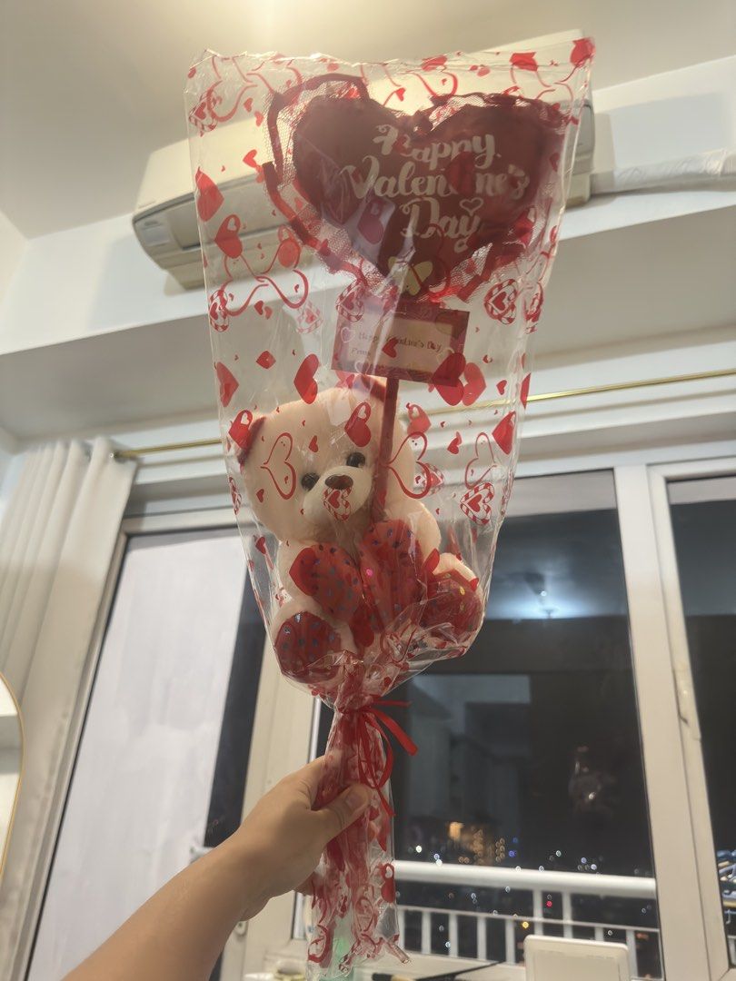 Valentine's Day Teddy Bear Bouquet (Category: Flowers & Bouquets) located in Taguig. Submitted by seek_and_ship (Listing ID 1432969623, Image 1). Description: - Adorable teddy bear bouquet for Valentine's Day. - Features a cute plush teddy bear holding a "Happy Valentine's Day" sign. - Beautifully wrapped in clear cellophane with heart patterns. - Tied with a festive red ribbon. - Includes a heart-shaped balloon. - A perfect and heartwarming gift