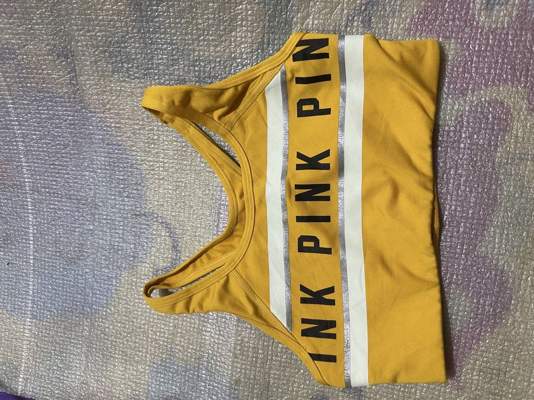 Pink Victoria's Secret Ultimate Sports Bra (Category: Activewear) located in Manila. Submitted by juanabanana (Listing ID 1433140958, Image 2). Description: Yellow sports bra from Pink Victoria's Secret. Features the brand name across the chest in black lettering with a white and silver stripe. The bra has a racerback design. Size is S/P (Small/Petite). The bra is made of a blend of polyester and spandex. Needs wash.