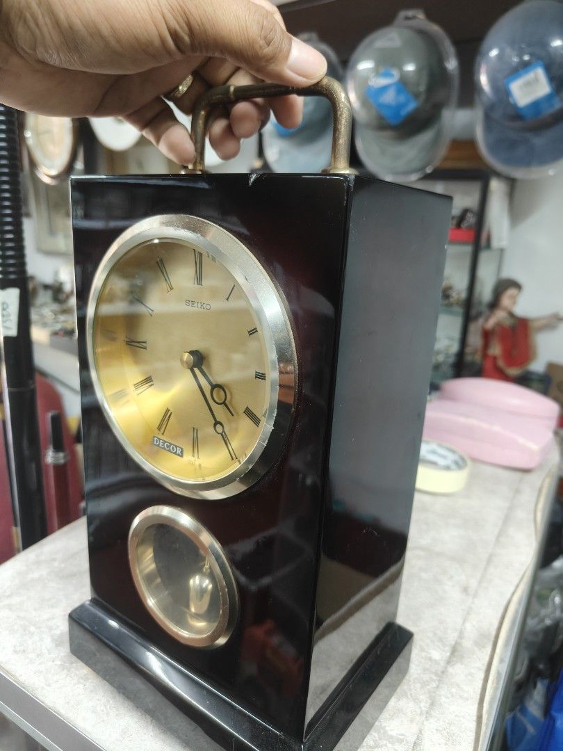 Seiko Decor Pendulum Clock (Category: Clocks) located in Cavite. Submitted by sevillajoh71978 (Listing ID 1433081465, Image 3). Description: - Vintage Seiko Decor pendulum clock - Gold-toned clock face with Roman numerals - Features a pendulum display - Dark wood finish with handle - Battery compartment and mechanism visible.