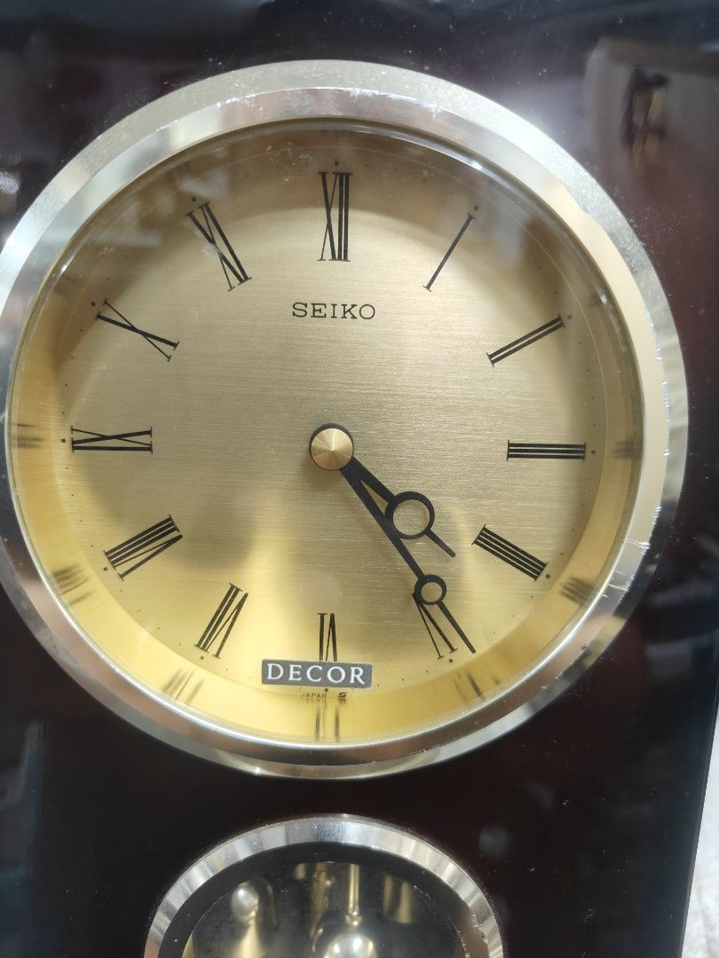 Seiko Decor Pendulum Clock (Category: Clocks) located in Cavite. Submitted by sevillajoh71978 (Listing ID 1433081465, Image 2). Description: - Vintage Seiko Decor pendulum clock - Gold-toned clock face with Roman numerals - Features a pendulum display - Dark wood finish with handle - Battery compartment and mechanism visible.