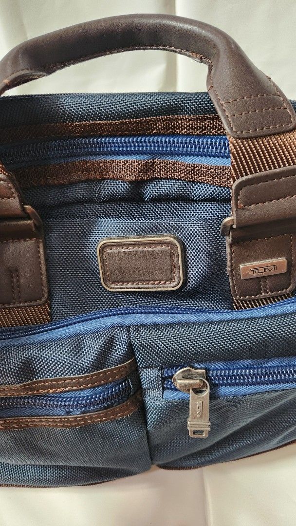 Tumi Alpha Bravo Briefcase (Category: Briefcases) located in Antipolo. Submitted by luislasi (Listing ID 1433145509, Image 3). Description: - Tumi Alpha Bravo Andersen briefcase - Navy blue exterior with brown leather accents - Detachable shoulder strap included - Multiple zippered compartments for secure storage - Interior features patterned lining - Top handle for easy carrying - Small hole on right buckle. Needs re-stiching but still usable.