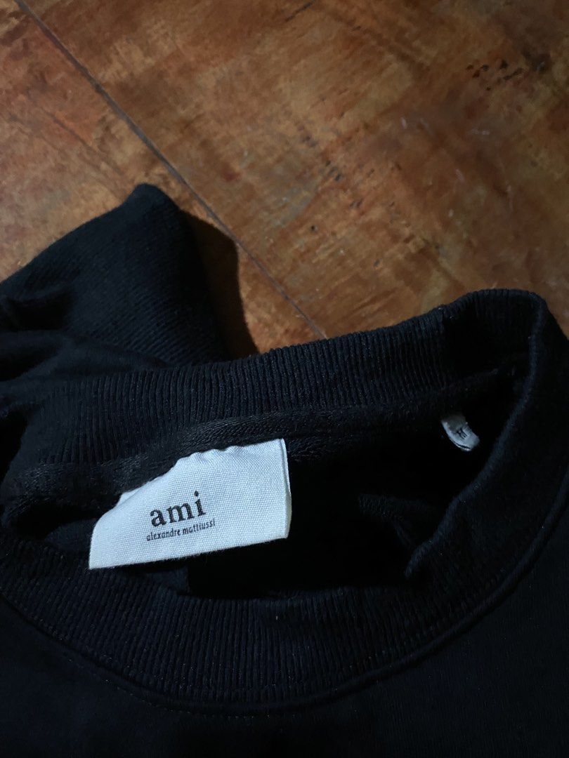 AMI Alexandre Mattiussi Black Sweatshirt (Category: Coats, Jackets and Outerwear) located in Dumaguete. Submitted by snatchthrift.co (Listing ID 1429752765, Image 3). Description: Black AMI Alexandre Mattiussi sweatshirt. Features the brand's signature Ami de Coeur logo on the chest. Made in Tunisia. The care label indicates the material is 100% organic cotton. Size tag is visible. Crew neck design..
