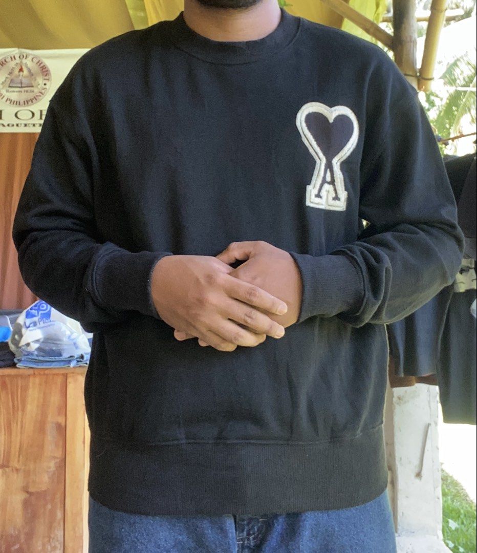 AMI Alexandre Mattiussi Black Sweatshirt (Category: Coats, Jackets and Outerwear) located in Dumaguete. Submitted by snatchthrift.co (Listing ID 1429752765, Image 2). Description: Black AMI Alexandre Mattiussi sweatshirt. Features the brand's signature Ami de Coeur logo on the chest. Made in Tunisia. The care label indicates the material is 100% organic cotton. Size tag is visible. Crew neck design..