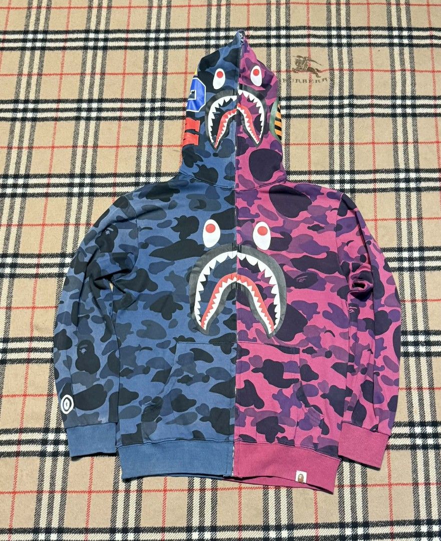 BAPE Camo Shark Hoodie (Category: Hoodies) located in Cavite. Submitted by markjoseph24866 (Listing ID 1429715011, Image 1). Description: BAPE hoodie features a unique split design with blue and pink camo patterns. It has the iconic shark face design on the hood. The hoodie has a full zip closure and ribbed cuffs and hem. The BAPE logo is visible on the sleeve. It's a stylish and eye-catching piece..
