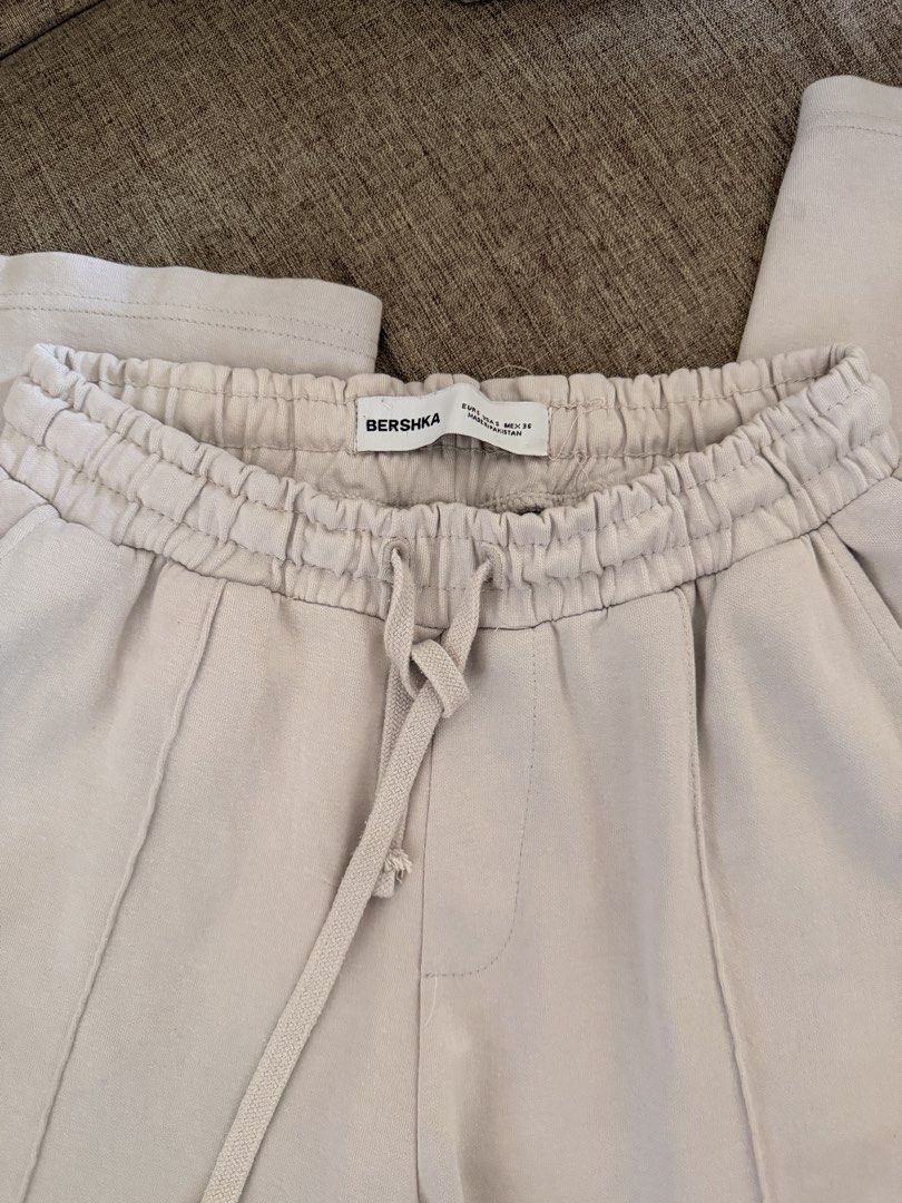 Bershka Beige Jogger Pants (Category: Joggers) located in Taguig. Submitted by johnjohnpaul (Listing ID 1429724240, Image 1). Description: Beige jogger pants from Bershka. Features an elastic waistband with a drawstring. The pants have a relaxed fit with vertical seams down the front. The cuffs are also elasticated. The size tag is visible in the image. Worn this several times. Still in very good condition..