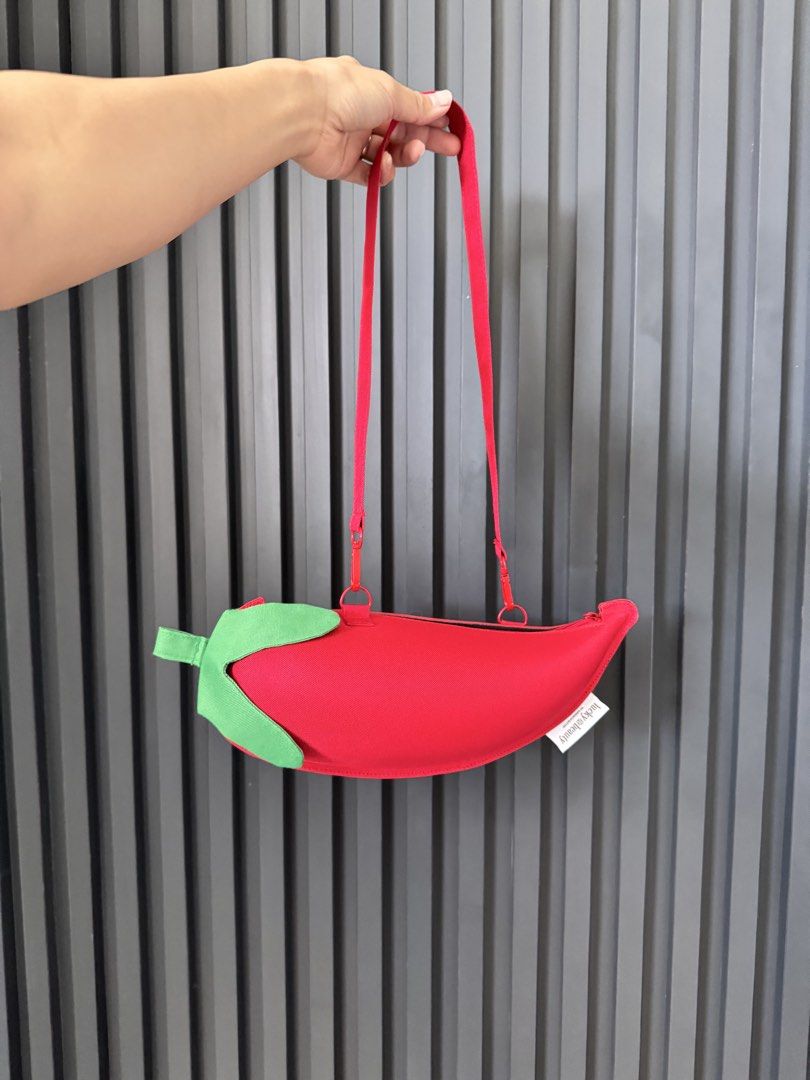 Chili Pepper Crossbody Bag (Category: Cross-body Bags) located in San Juan City. Submitted by steffchua (Listing ID 1429679782, Image 1). Description: Unique crossbody bag shaped like a chili pepper. Features a red exterior with a green leaf detail. Includes a long red strap and a zipper closure. A small tag is visible on the side. Perfect for adding a fun touch to any outfit..