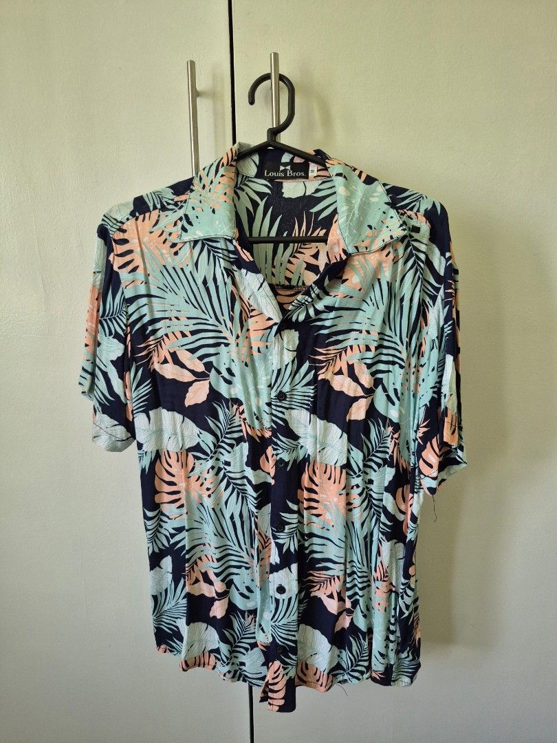 Floral Print Button-Down Shirt (Category: Shirts) located in Valenzuela. Submitted by pappx (Listing ID 1429767633, Image 1). Description: Button-down shirt features a vibrant floral print in shades of blue, peach, and green. It has a collared neckline and long sleeves. The shirt is hanging on a black hanger..