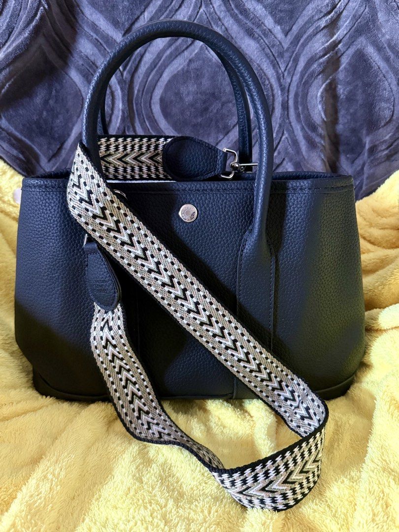 Hermes Garden Party Tote Bag (Category: Luxury Bags & Wallets) located in Quezon City. Submitted by lailah00 (Listing ID 1429774674, Image 2). Description: Black tote bag with a patterned shoulder strap. Features a silver Hermes Paris logo on the front. The interior has a zippered pocket and a light-colored lining. Includes a detachable shoulder strap. The bag has a structured shape with top handles..