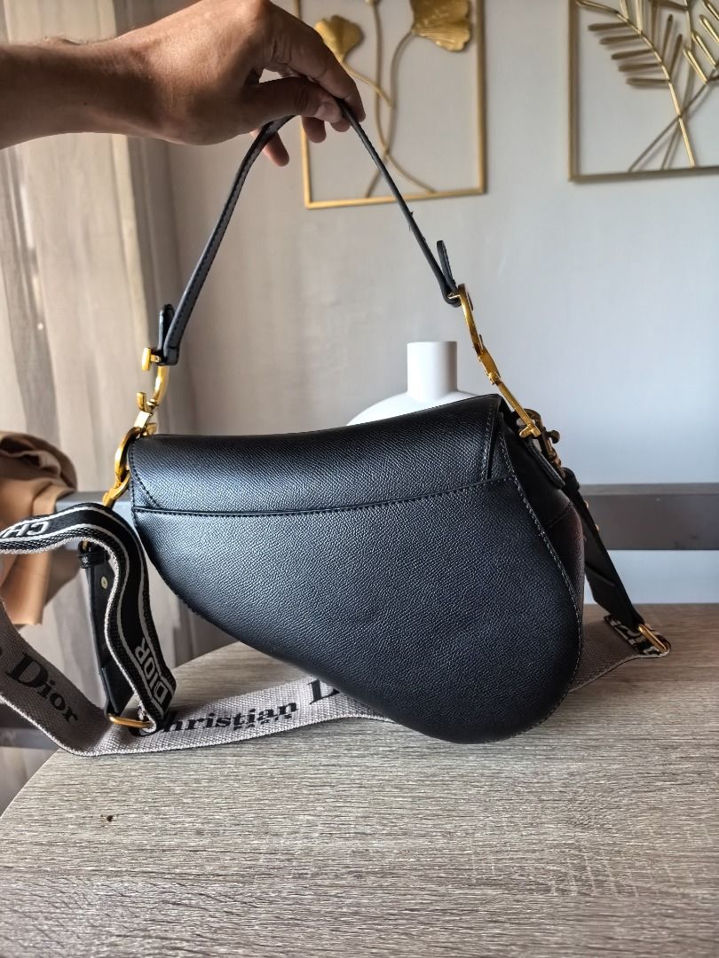 Japan Surplus Dior Saddle Bag Black (Category: Luxury Bags & Wallets) located in Cebu City. Submitted by esrpreloved (Listing ID 1429829227, Image 3). Description: Black Dior Saddle bag with a detachable shoulder strap. Features a 'D' charm and gold-tone hardware. The strap has 'Christian Dior' lettering. The bag is held by a hand in the image..