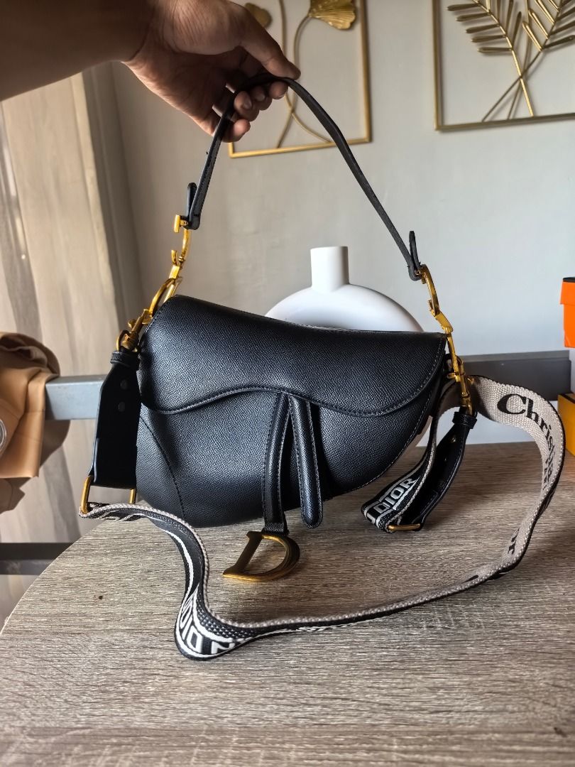 Japan Surplus Dior Saddle Bag Black (Category: Luxury Bags & Wallets) located in Cebu City. Submitted by esrpreloved (Listing ID 1429829227, Image 1). Description: Black Dior Saddle bag with a detachable shoulder strap. Features a 'D' charm and gold-tone hardware. The strap has 'Christian Dior' lettering. The bag is held by a hand in the image..