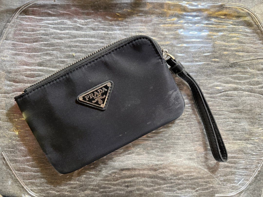 Prada Black Wristlet Pouch (Category: Luxury Bags & Wallets) located in Taytay. Submitted by jayezapanta (Listing ID 1429834212, Image 2). Description: Black Prada wristlet pouch. Features a silver-tone zipper and a wrist strap. The Prada logo is visible on the front. The interior has a small pocket. The lining has a Prada logo pattern. Needs cleaning Not auth No rubs or tears.