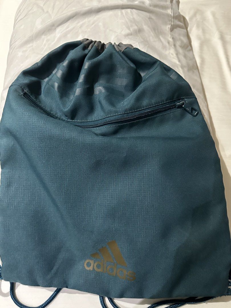 Adidas Drawstring Bag (Category: Backpacks) located in Manila. Submitted by qualitypreluvd (Listing ID 1433342644, Image 1). Description: - Adidas teal drawstring bag - Gold Adidas logo - Zippered front pocket - Drawstring closure - Small hanging loop - Adidas logo on zipper - Ideal for gym clothes and essentials.