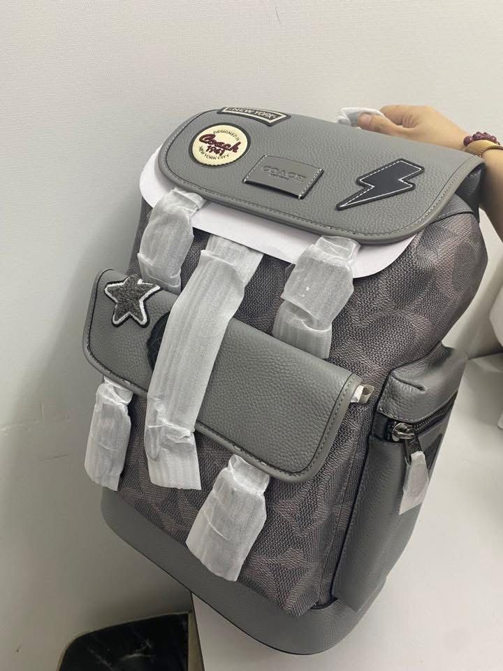 Coach Patchwork Backpack (Category: Bags & Wallets) located in Petaling Jaya. Submitted by angah_75 (Listing ID 1433352864, Image 1). Description: - Authentic Coach backpack - Grey leather exterior - Features multiple patches (star, lightning bolt) - Signature Coach pattern - Flap closure - Zippered front pocket - Adjustable shoulder straps - Breathable mesh back panel - Coach logo detail - Small zippered side pocket.