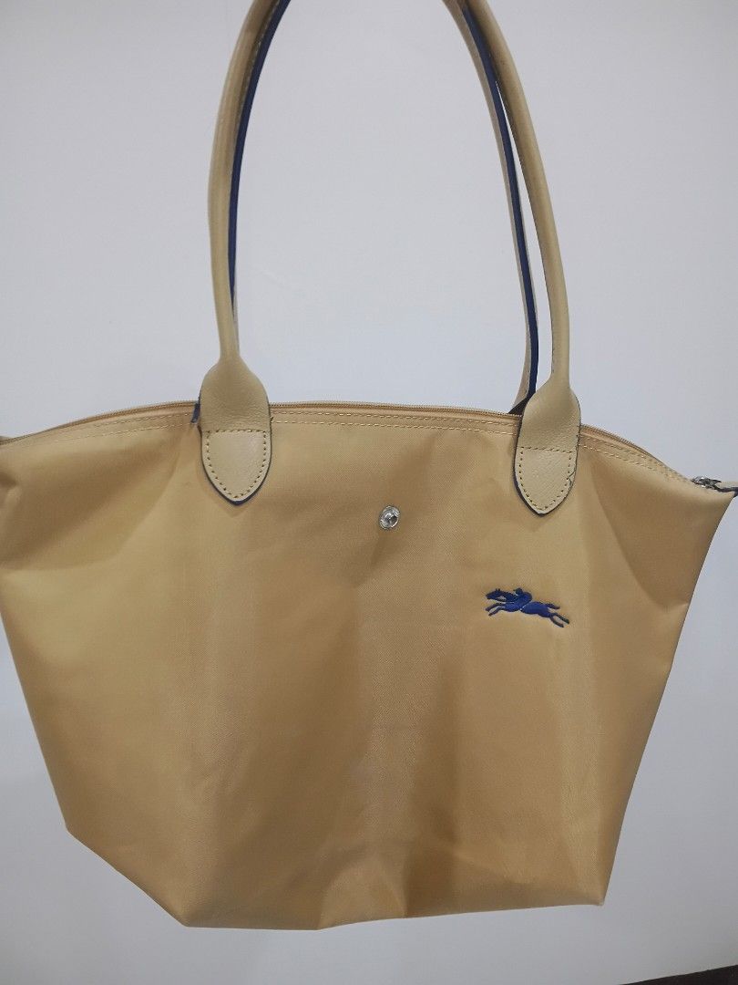 Longchamp Le Pliage Tote Bag (Category: Luxury Bags & Wallets) located in Manila. Submitted by daisuki8 (Listing ID 1433395097, Image 1). Description: - Authentic Longchamp Le Pliage tote bag - Color: Beige - Features the iconic blue horse logo - Secure zipper closure - Beige leather handles with blue accents - Interior: White lining with a small pocket - Snap closure - Longchamp logo on zipper pull -issue: rubber lining on handle as shown in pic