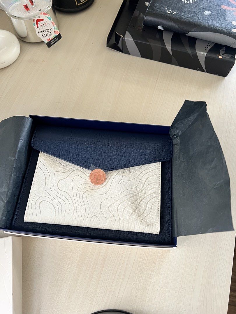 Starbucks Clutch with Coin (Category: Clutches) located in Makati City. Submitted by esila.essentials (Listing ID 1433392029, Image 2). Description: - Starbucks clutch - White topographic design - Navy blue flap - Includes a coin - Comes in a Starbucks box - Gift set.