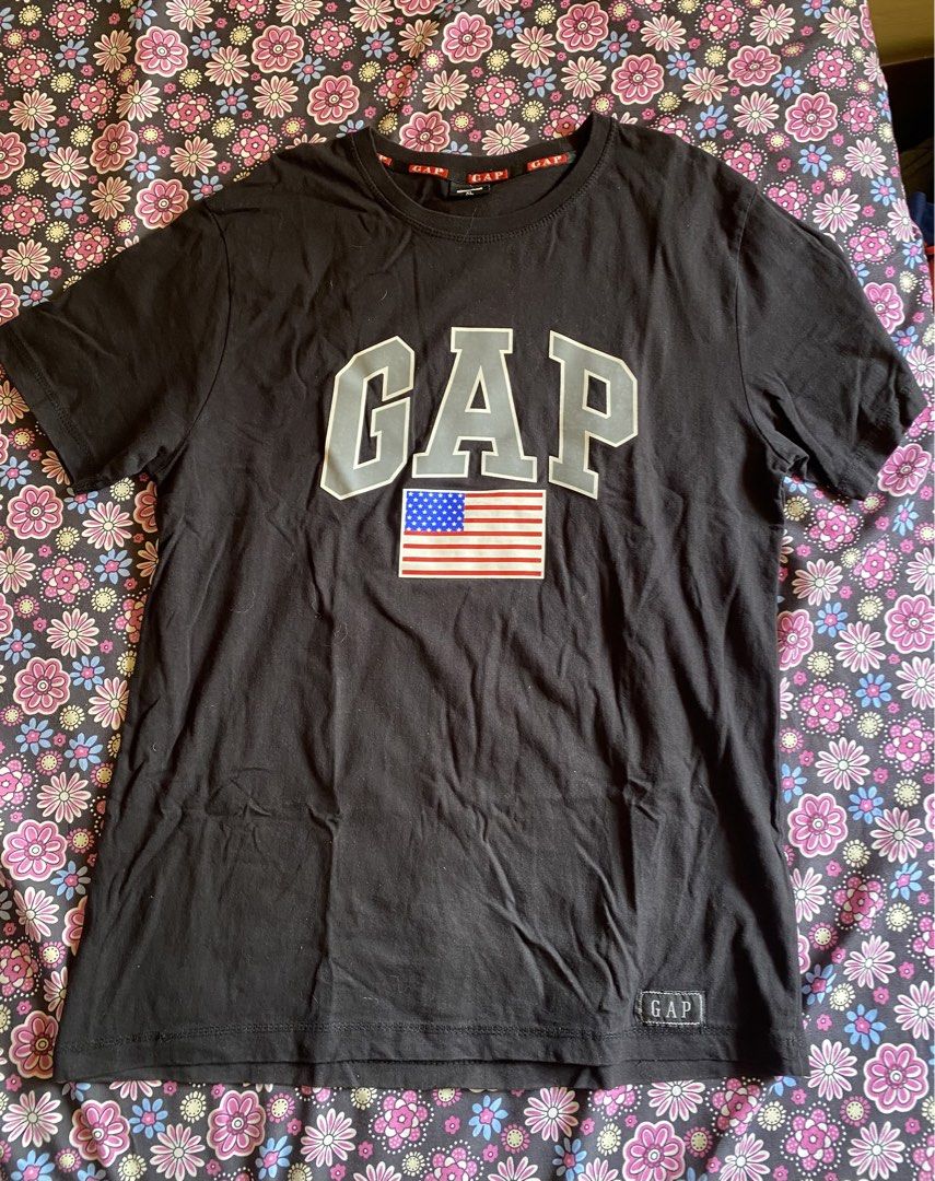 GAP Black T-shirt with American Flag (Category: Tshirts & Polo Shirts ) located in Manila. Submitted by kathhhhh236 (Listing ID 1433546913, Image 1). Description: - Black GAP t-shirt - Features a large "GAP" logo and American flag graphic - GAP logo on sleeve and neckline - Size: XL - Material: 100% cotton - Made in Bangladesh.