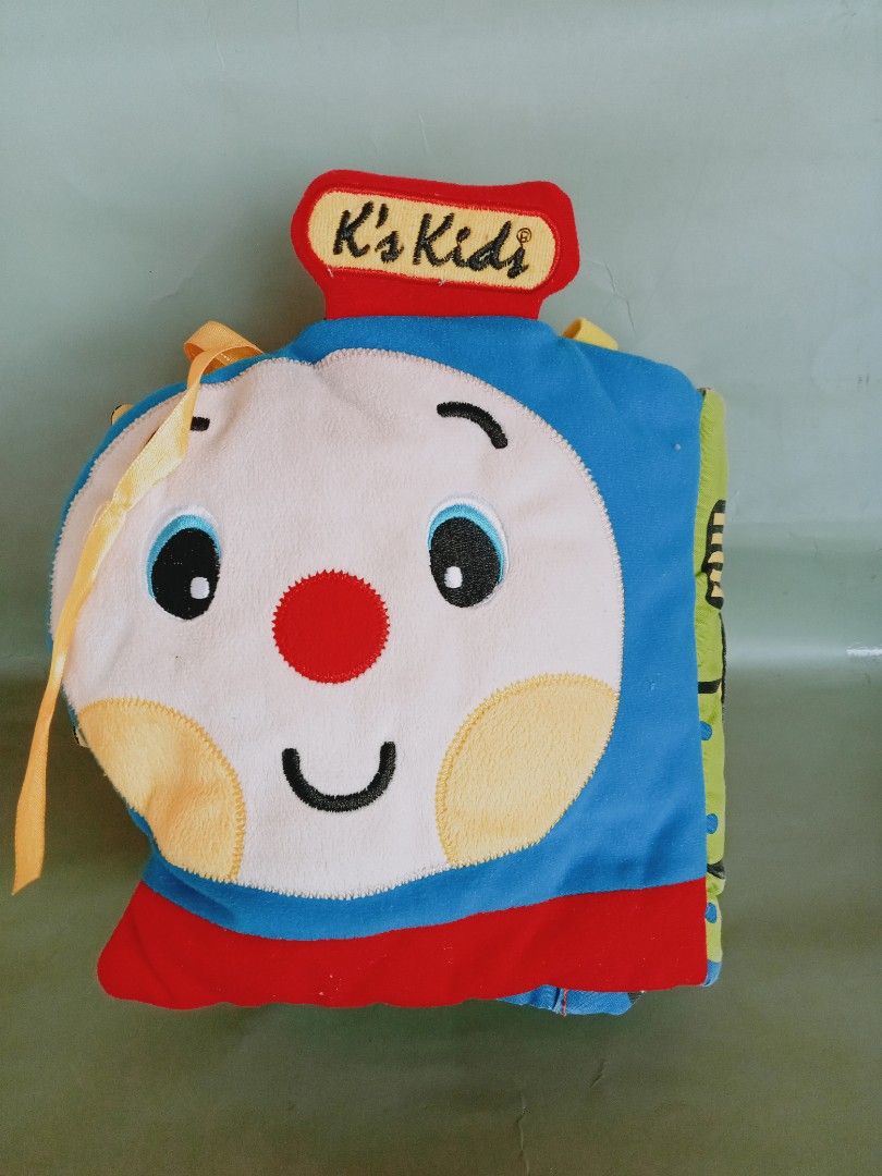 K's Kids Train Soft Book (Category: Infant Playtime) located in Rosario. Submitted by elysedeclutter (Listing ID 1433444008, Image 2). Description: K's Kids soft book is shaped like a train. It features colorful illustrations and interactive elements, including a mirror, a flower-shaped teether, and removable food cutouts. The book has different compartments with various pictures and textures to engage a baby's senses. It is designed to be soft a