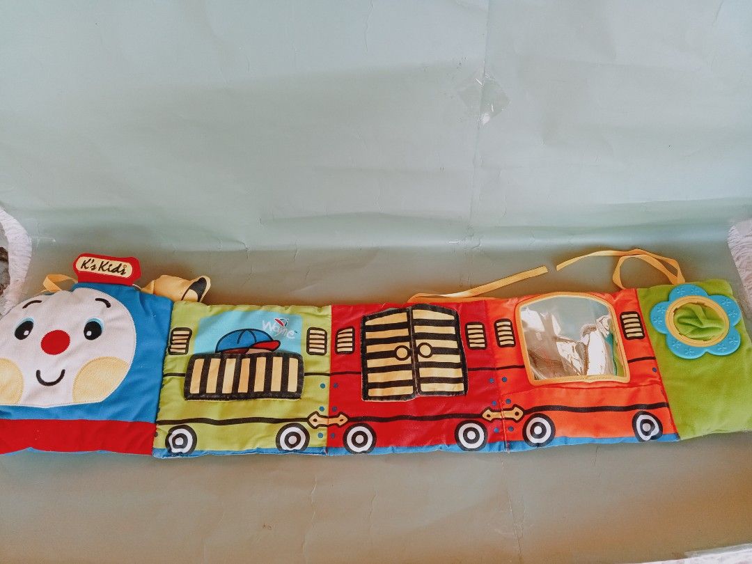 K's Kids Train Soft Book (Category: Infant Playtime) located in Rosario. Submitted by elysedeclutter (Listing ID 1433444008, Image 1). Description: K's Kids soft book is shaped like a train. It features colorful illustrations and interactive elements, including a mirror, a flower-shaped teether, and removable food cutouts. The book has different compartments with various pictures and textures to engage a baby's senses. It is designed to be soft a