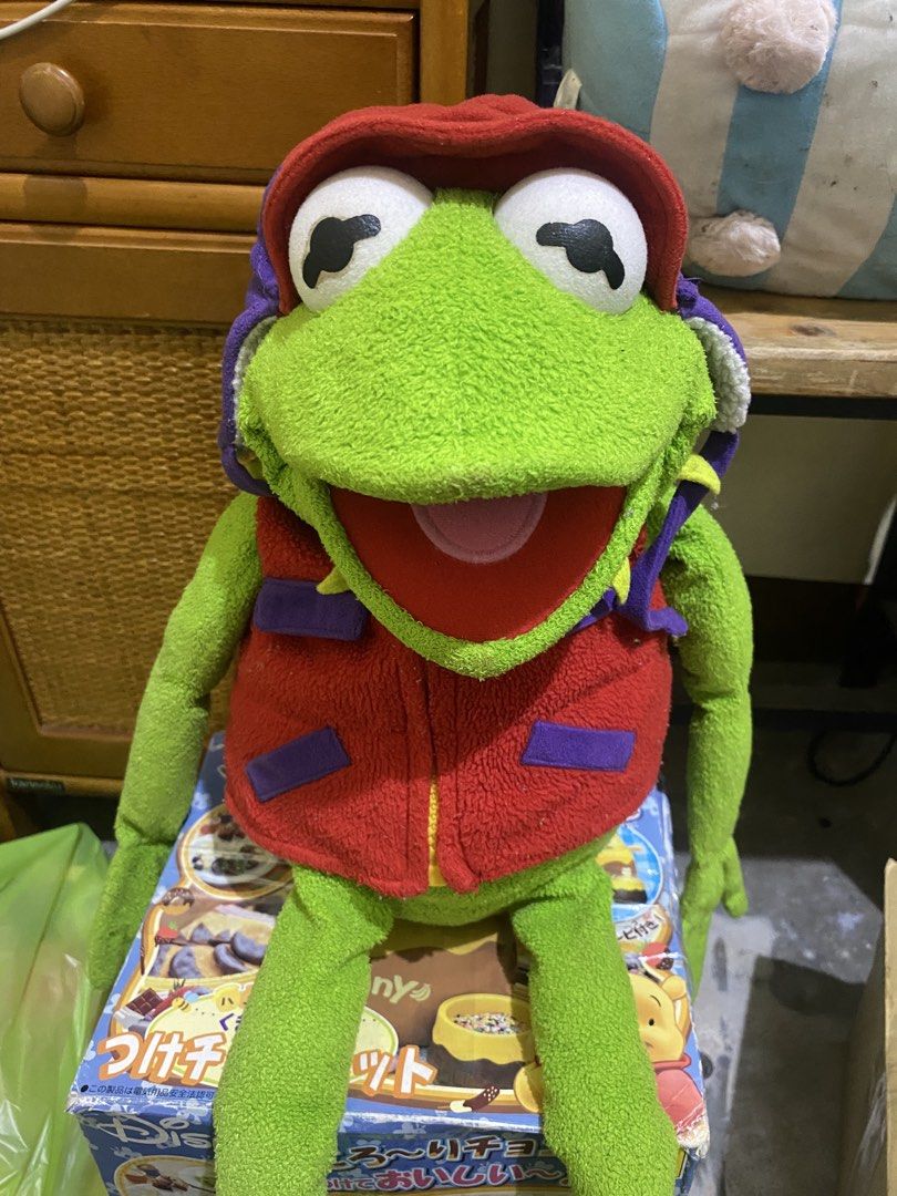 Kermit the Frog-tographer Plush Toy (Category: Plushies & Soft Toys) located in Imus. Submitted by mnmv23 (Listing ID 1433668452, Image 2). Description: - Kermit the Frog plush toy - Features a red vest and hat - Designed by The Jim Henson Company - Green skin and large eyes - Sitting on a box - Long arms and legs - missing camera.