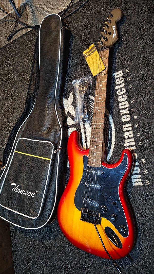 Thomson Electric Guitar with Case electric guitar (Category: Musical Instruments) located in Pasig City. Submitted by tupriomichaeljohn (Listing ID 1433661993, Image 2). Description: - Thomson electric guitar - Sunburst finish - Includes gig bag and cable - Tremolo system - Three pickups - Rosewood fretboard - Black pickguard - Thomson logo on headstock.