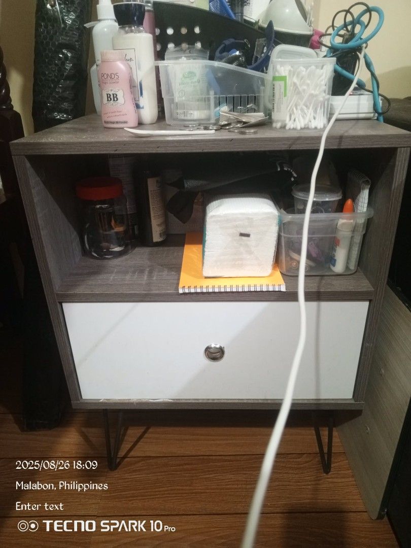 Wooden Nightstand with Drawer (Category: Shelves, Cabinets & Racks) located in Manila. Submitted by melvox (Listing ID 1433768940, Image 1). Description: - Nightstand with drawer and open shelf - White drawer front - Gray top and sides - Metal hairpin legs - Minor wear on top edge - Ideal for bedroom or living room.