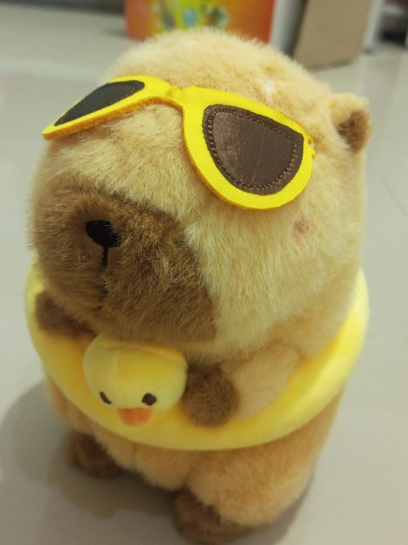 Capybara Plush Toy with Sunglasses (Category: Plushies & Soft Toys) located in Manila. Submitted by kb_kg (Listing ID 1433790453, Image 1). Description: - Adorable capybara plush toy - Wearing sunglasses and a yellow floatie - Includes a small duck attached to the floatie - Light brown and beige color scheme - Comes with a tag - Perfect for collectors or as a gift.
