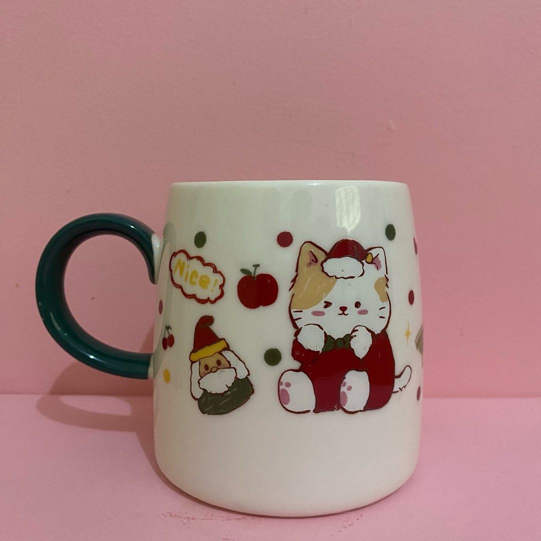 Christmas Cat Mug with Green Handle (Category: Coffee & Tea Tableware) located in Manila. Submitted by hellovalleygirl (Listing ID 1433888179, Image 1). Description: - Adorable Christmas mug. - Features a cute cat design. - White mug with a green handle. - Decorated with a cat in a Santa suit, an apple, and the word "Nice!". - Perfect for hot beverages..