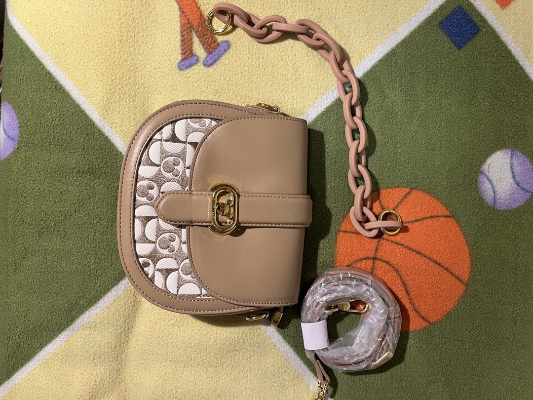 Crossbag saddle bag (DISNEY X COACH) (Category: Luxury Bags & Wallets) located in Caloocan City. Submitted by lawrence.jay (Listing ID 1433885300, Image 2). Description: Coach saddle bag features a unique Mickey Mouse pattern on the front. It has a tan leather exterior with a gold-tone clasp and hardware. The bag comes with a detachable shoulder strap and a chain strap. The design is a collaboration with Disney..