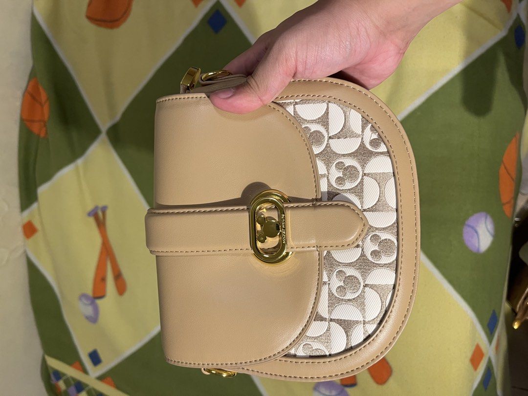 Crossbag saddle bag (DISNEY X COACH) (Category: Luxury Bags & Wallets) located in Caloocan City. Submitted by lawrence.jay (Listing ID 1433885300, Image 1). Description: Coach saddle bag features a unique Mickey Mouse pattern on the front. It has a tan leather exterior with a gold-tone clasp and hardware. The bag comes with a detachable shoulder strap and a chain strap. The design is a collaboration with Disney..