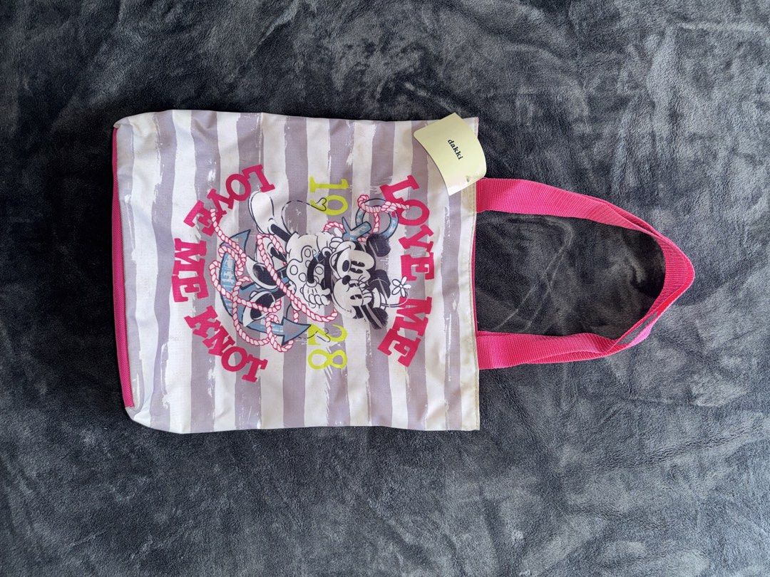 Dakki Love Me Knot Tote Bag (Category: Tote Bags) located in Manila. Submitted by chaooo25 (Listing ID 1433806754, Image 1). Description: - Dakki tote bag with a fun Mickey and Minnie Mouse design. - Features a pink handle and a striped background. - Adorned with "Love Me Knot" and the number "1928". - Perfect for carrying your essentials in style..