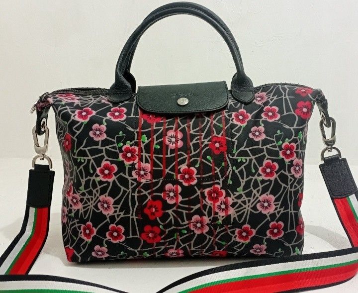 Longchamp Floral Printed Pliage MEDIUM Handbag with Shoulder Strap (Category: Luxury Bags & Wallets) located in Manila. Submitted by eriiicaspage (Listing ID 1433888964, Image 2). Description: PreOwned Lightly Used Longchamp handbag with a striking floral pattern on a black background. - Features a classic top handle and a detachable shoulder strap with red, white, and green stripes. - Secure flap closure with a snap and a silver-tone zipper. - I