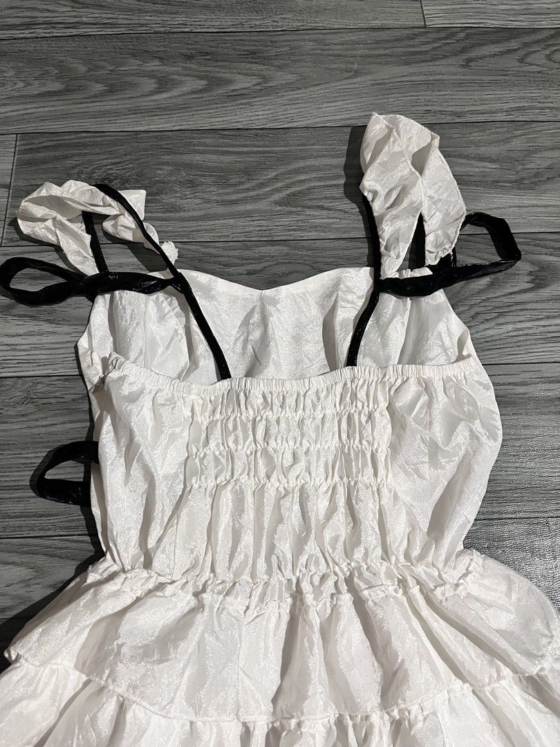 White Ruffled Dress with Black Accents (Category: Dresses) located in Pasig City. Submitted by anya2000 (Listing ID 1433903076, Image 2). Description: - White dress with a playful ruffled skirt. - Contrasting black accents on straps, neckline, and sleeves. - Unique design with black detailing. - Comfortable fit with an elasticated back. - Made from a lightweight, potentially sheer fabric..