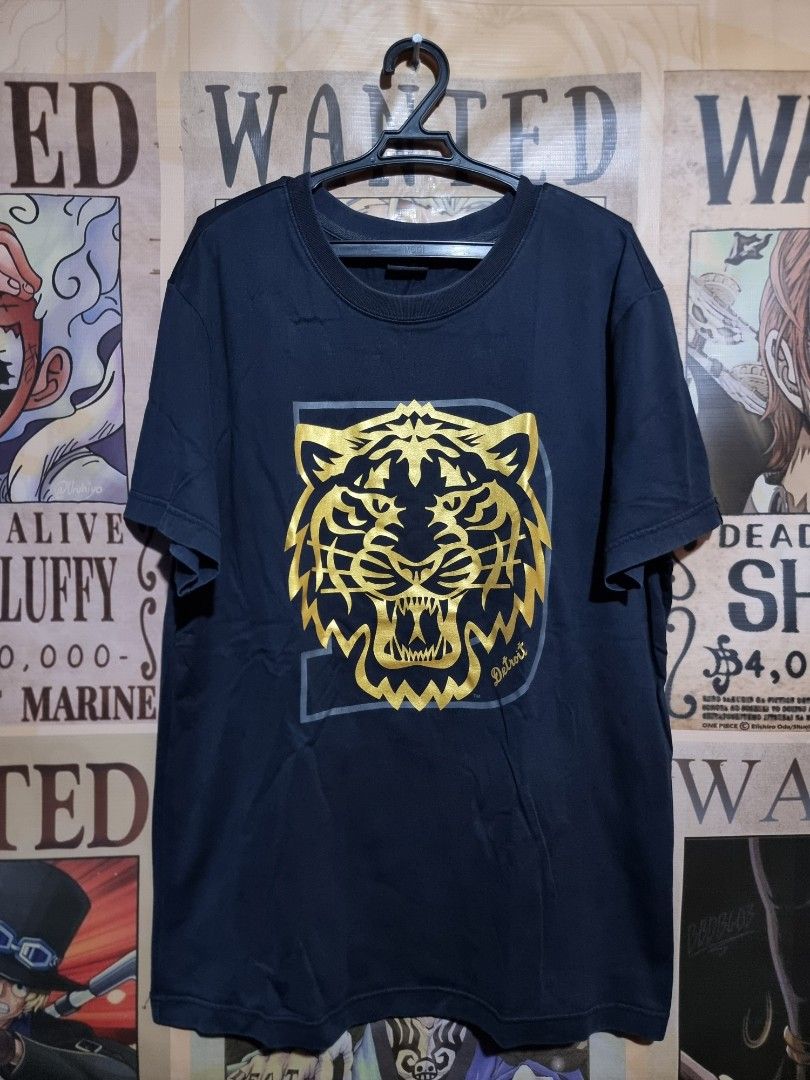 MLB Detroit Tigers Graphic Tee - Large (Category: Tshirts & Polo Shirts ) located in Imus. Submitted by aim_for_less (Listing ID 1434117562, Image 2). Description: MLB Detroit Tigers Graphic Tee Features a striking gold tiger design on a navy blue background. It has a crew neck and short sleeves. The tag indicates it is a size Large (175/92A). Made by MLB (Major League Baseball) -DIMES: 21" X 29" - COLOR RATE: 9.7/10 - NO ISSUE - VERY GOOD CONDIT