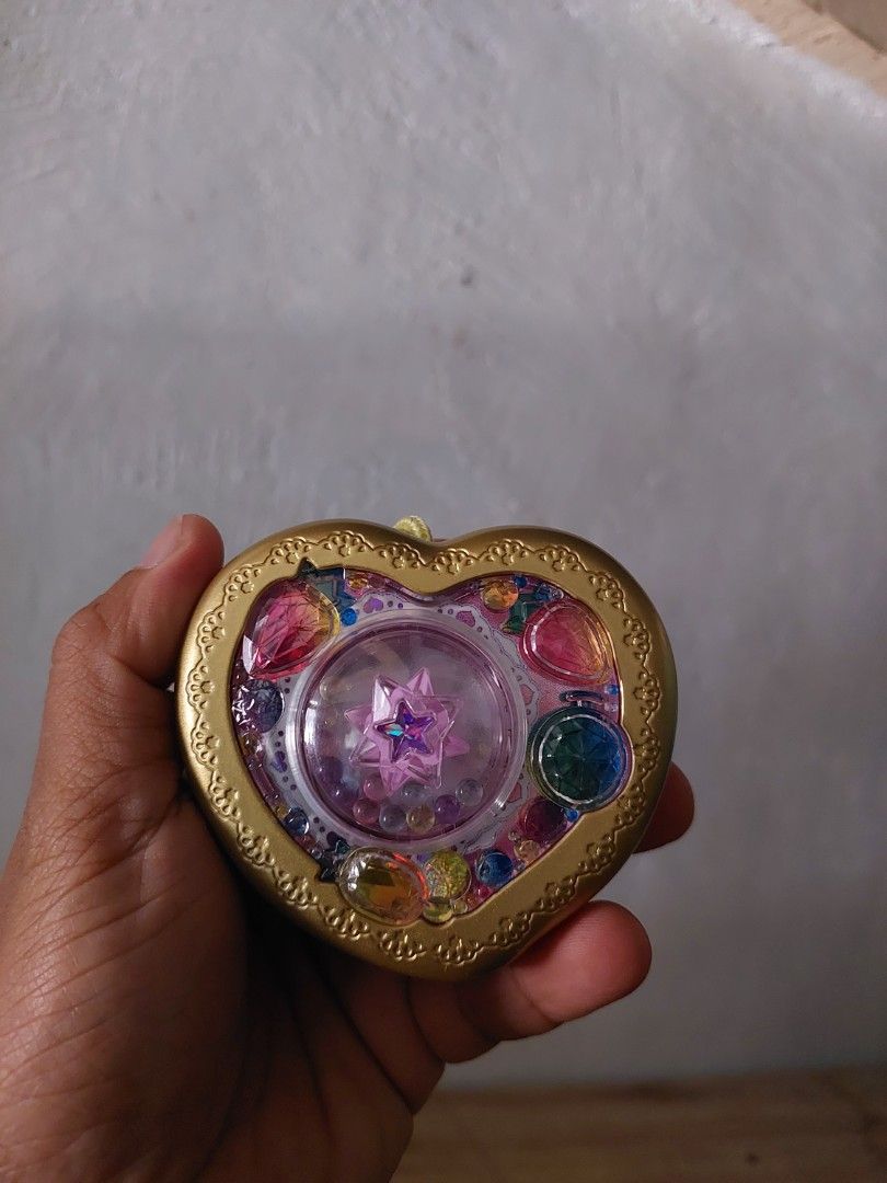 Bandai Heart-Shaped Toy (Category: Kids Toys) located in Quezon City. Submitted by jpnvintageonline (Listing ID 1434213794, Image 3). Description: - Heart-shaped toy with gold frame - Adorned with colorful gems and a star design - Pink back with battery compartment - Includes a yellow string - Made in Thailand by Bandai.