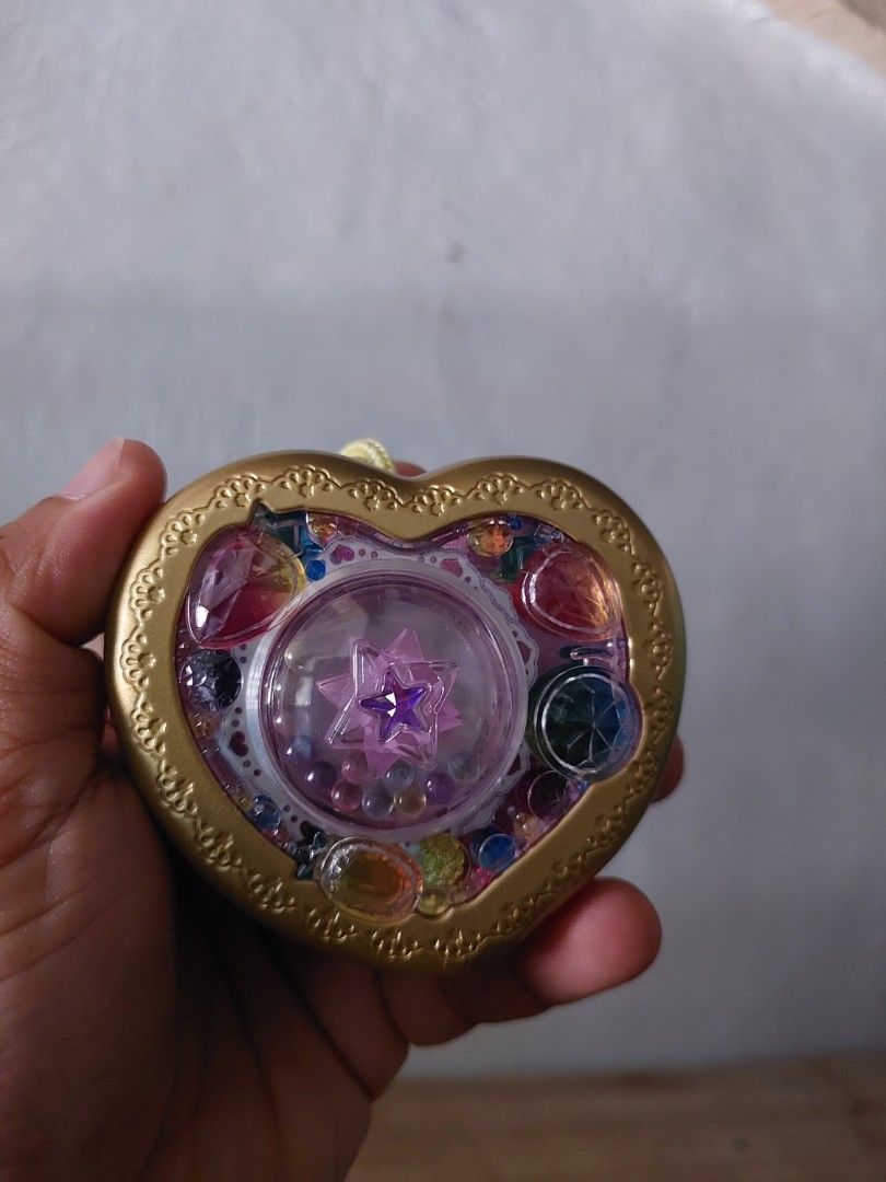 Bandai Heart-Shaped Toy (Category: Kids Toys) located in Quezon City. Submitted by jpnvintageonline (Listing ID 1434213794, Image 1). Description: - Heart-shaped toy with gold frame - Adorned with colorful gems and a star design - Pink back with battery compartment - Includes a yellow string - Made in Thailand by Bandai.