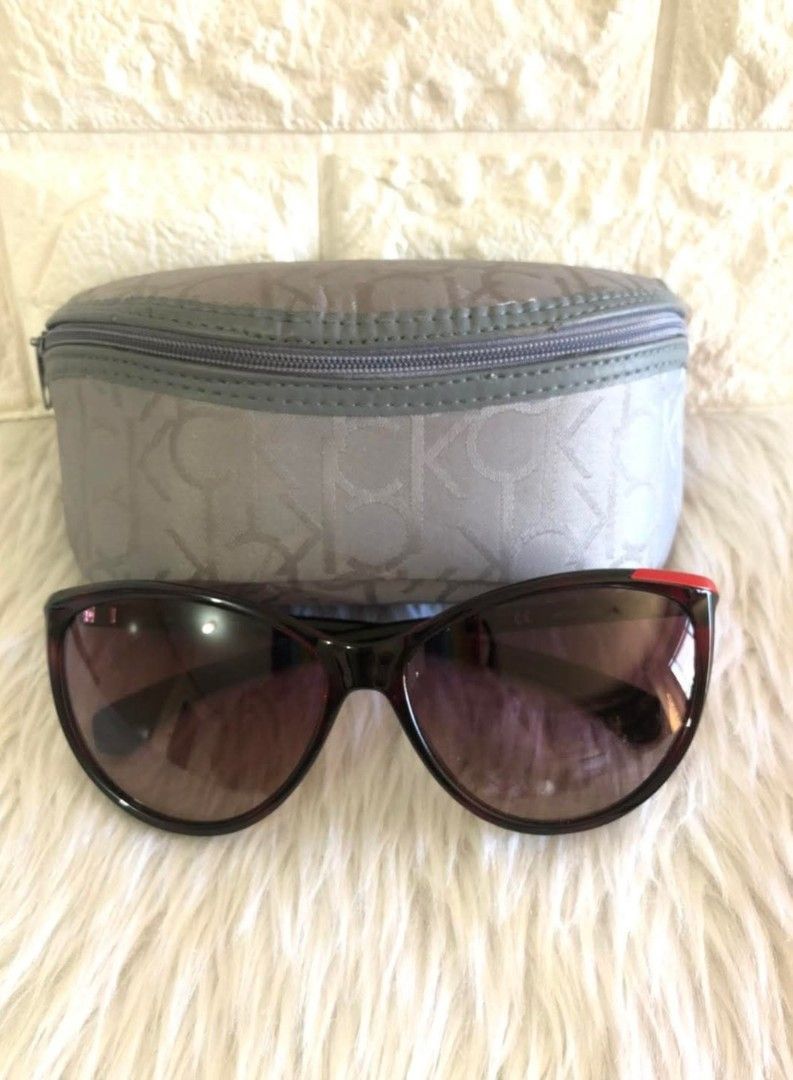 Calvin Klein Sunglasses with Case (Category: Sunglasses & Eyewear) located in Cavite. Submitted by geturs (Listing ID 1434255339, Image 1). Description: - Calvin Klein sunglasses - Dark frame with tinted lenses - Gray case with Calvin Klein logo - Red accent on the frame - Stylish eye protection.