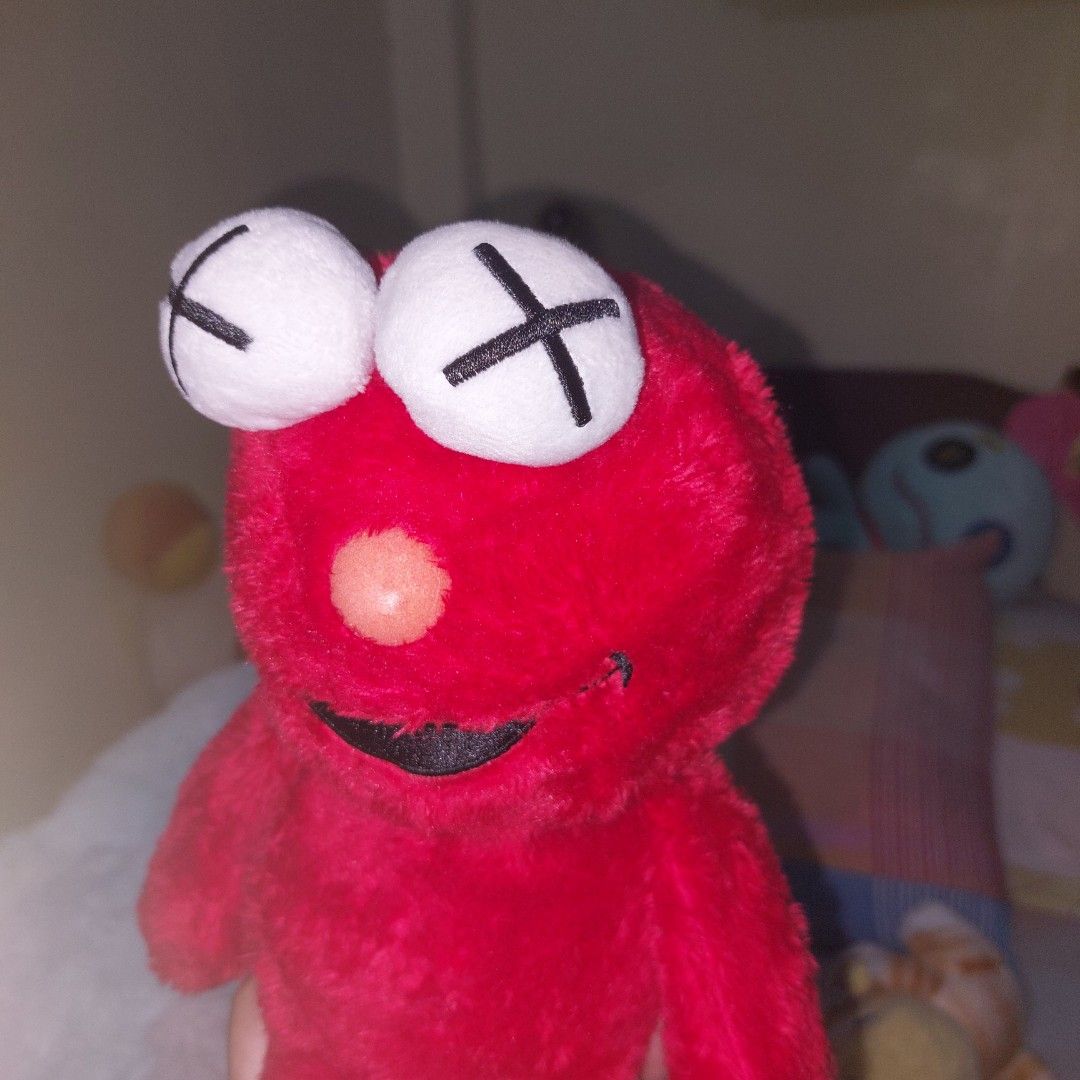 Elmo Kaws - no etiketa (Category: Plushies & Soft Toys) located in Mandaluyong City. Submitted by 13thsilverrabbit (Listing ID 1434188961, Image 2). Description: Unique red plush toy features distinctive white eyes with black "X" markings. It has a smiling black mouth and a small orange nose. The toy is soft and plush, with a distinctive shape..