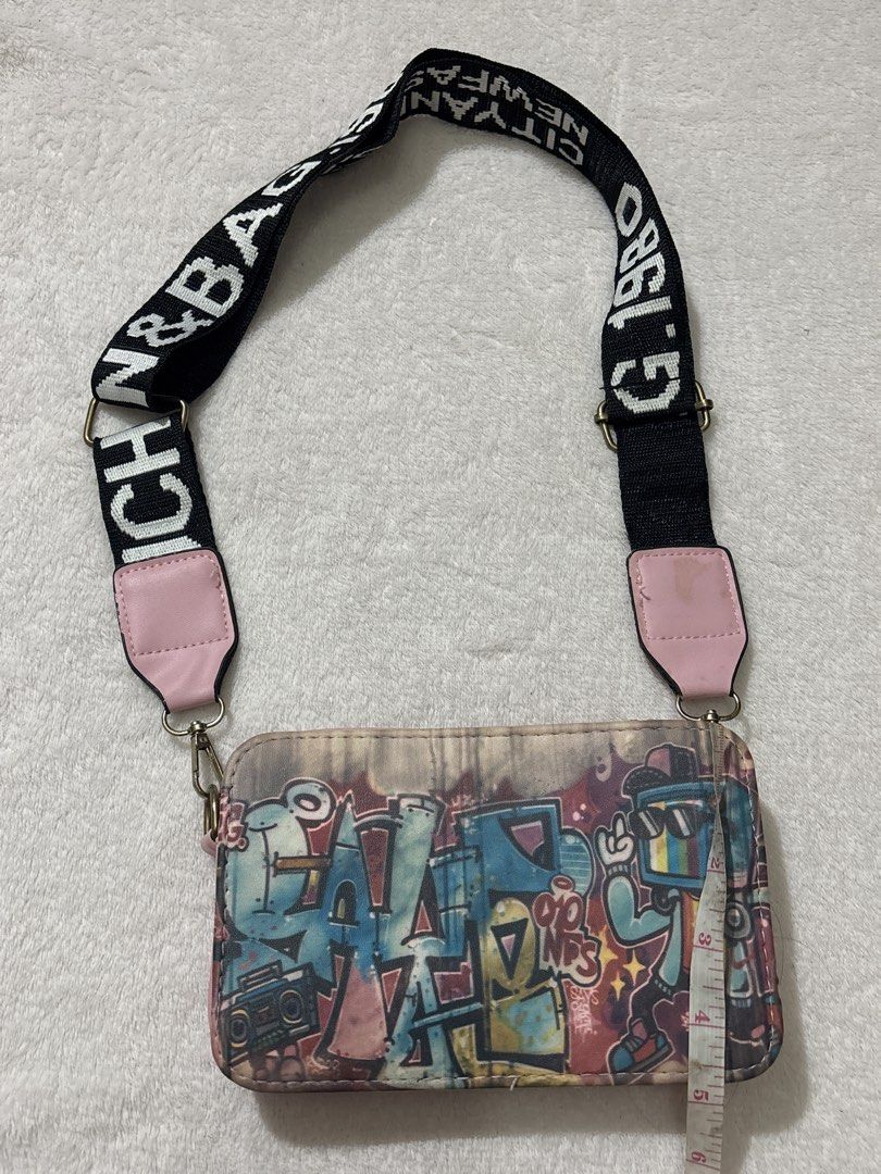 Graffiti Print Crossbody Bag (Category: Cross-body Bags) located in Muntinlupa City. Submitted by findsbymina (Listing ID 1434362439, Image 3). Description: Original Price: Approximately P700 Measurements: Length: 7.5 inches Width: 4.7 inches Description: This is a Bench Graffiti Street Art Crossbody Bag. It features a “guitar strap” style handle, which was a major trend in the mid-to-late 2010s and has recently made a comeback with the Y2K/Retro