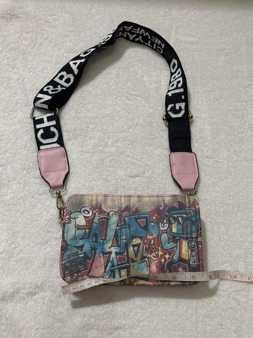 Graffiti Print Crossbody Bag (Category: Cross-body Bags) located in Muntinlupa City. Submitted by findsbymina (Listing ID 1434362439, Image 2). Description: Original Price: Approximately P700 Measurements: Length: 7.5 inches Width: 4.7 inches Description: This is a Bench Graffiti Street Art Crossbody Bag. It features a “guitar strap” style handle, which was a major trend in the mid-to-late 2010s and has recently made a comeback with the Y2K/Retro