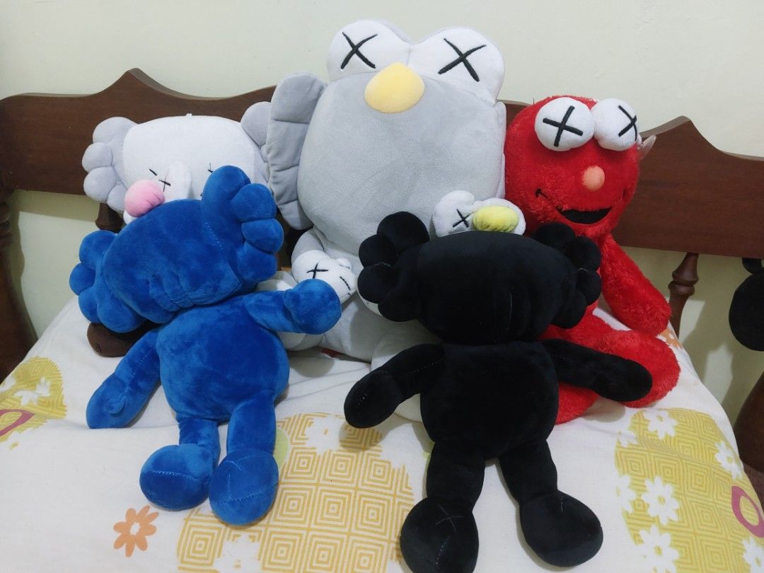 KAWS Plush Toys (Category: Plushies & Soft Toys) located in Mandaluyong City. Submitted by 13thsilverrabbit (Listing ID 1434189900, Image 1). Description: Collection of KAWS plush toys in various colors. Includes blue, black, white, gray, and brown figures. Also includes a red Elmo-like plush toy with X eyes. These plush toys are soft and cuddly, perfect for display or as a gift..