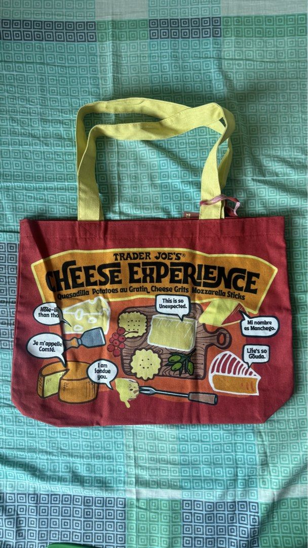 Trader Joe's Cheese Experience Tote Bag (Category: Tote Bags) located in Binan City. Submitted by nice_box (Listing ID 1434197387, Image 1). Description: - Trader Joe's "Cheese Experience" tote bag - Made of heavy-duty 100% cotton - Reinforced at stress points - Machine washable - Dimensions: Approximately 14 inches (H) x 19 inches (W) - Features yellow handles and a red body with cheese-themed graphics.