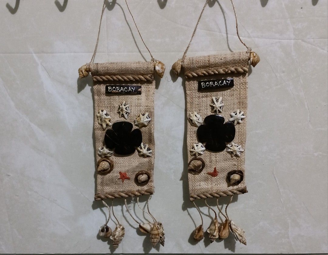 Boracay Shell Wall Hanging Decor / Handmade Set of 2 (Category: Wall Decor) located in Bulacan. Submitted by honhonliz (Listing ID 1434502736, Image 1). Description: - Unique wall hangings with a beach theme. - Features a burlap base. - Adorned with shells and a central black design. - Includes the word "BORACAY". - Decorated with a rope border and hanging shells. - Comes with a hanging string. - Ideal for adding a coastal touch to your home..