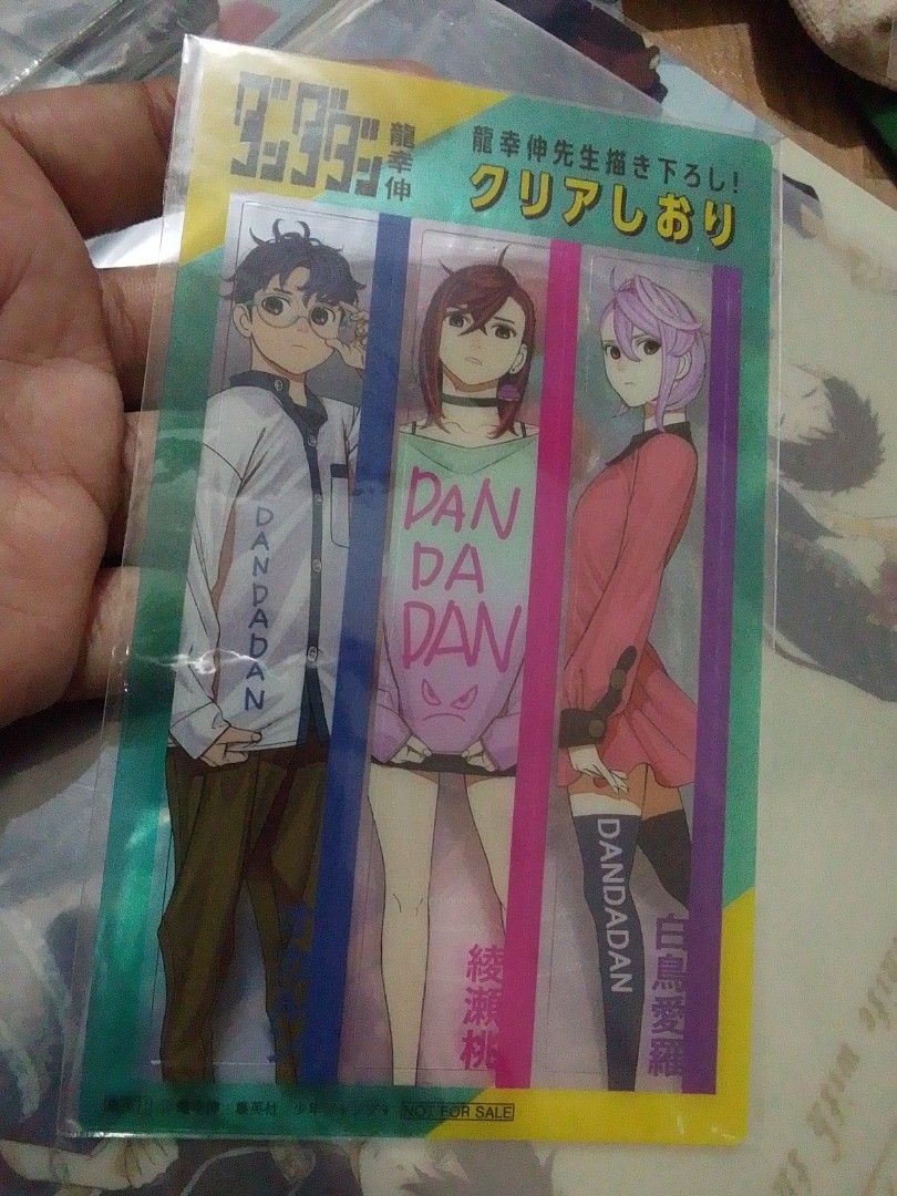 Dandadan Anime Bookmark (Category: Character Goods) located in Santa Rosa. Submitted by animemerchcollection (Listing ID 1434577792, Image 1). Description: - Dandadan anime bookmark - Features three characters - Clear bookmark with a colorful design - Includes Dandadan logo and character names - Brand new - In original packaging.